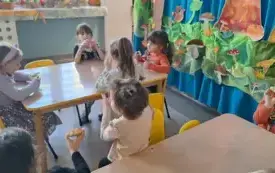 dzieci w strojach z akcentami dyniowymi i hallowenowymi siedzą przy stoliku i jedzą kolorowe donaty 