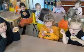 dzieci w strojach z akcentami dyniowymi i hallowenowymi siedzą przy stoliku i jedzą kolorowe donaty 