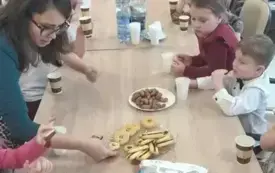 dzieci wraz z panią siedzą wzdłuż stołu na talerzykach leżą słodycze 