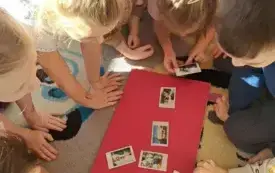 dzieci w klasie pochylone nad czerwonym kartonem na kt&oacute;rym leżą zdjęcia