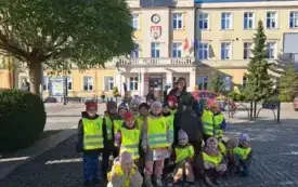 grupa dzieci w kamizelkach odblaskowych wraz z panią pozuje do zdjęcia z figurą pomnikiem jeża w tle widać Urząd Miasta Zgierza