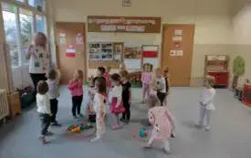dzieci wraz z panią stoją na dywanie na kt&oacute;rym leżą dwa okręgi a w nich kolorowe piłeczki