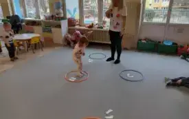 na dywanie leżą okręgi w nich papierowe st&oacute;pki ułożone w r&oacute;żny spos&oacute;b dziewczynka stoi w jednym z okręg&oacute;w pani stoi przed dziewczynką 