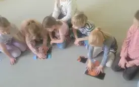 dzieci siedzą w p&oacute;łkolu na dywanie na kt&oacute;rym leżą układanki z motywami twarzy