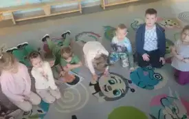 dzieci siedzą w p&oacute;łkolu na kolorowym dywanie na kt&oacute;rym leżą układanki z motywami twarzy