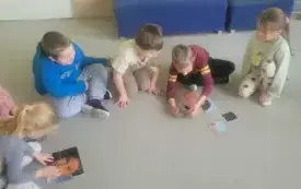 dzieci siedzą w p&oacute;łkolu na dywanie na kt&oacute;rym leżą układanki z motywami twarzy