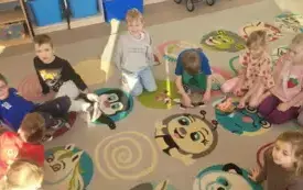 dzieci siedzą w p&oacute;łkolu na kolorowym dywanie na kt&oacute;rym leżą układanki z motywami twarzy