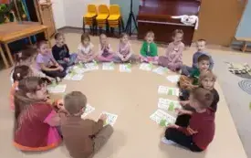 dzieci siedzą w kole na podłodze przed nimi leżą kartki z cyframi
