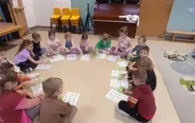 dzieci siedzą w kole na podłodze przed nimi leżą kartki z cyframi