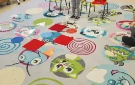 dwie dziewczynki stoją przy krzesełkach przy każdej trzy krzesełka na dywanie leżą kolorowe figury geometryczne