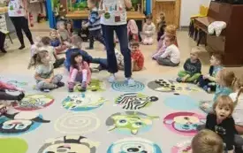 pani stoi i pokazuje dyplom dzieci siedzą dookoła na dywanie 