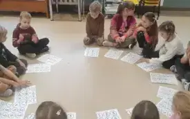 dzieci siedzą w kręgu na podłodze przed nimi leżą kartki z numerkami