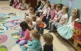 dzieci siedzą wzdłuż na ławeczkach na dywanie leżą kolorowe obręcze