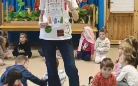 pani stoi i pokazuje dyplom dla grupy 3 na dywanie siedzą dzieci