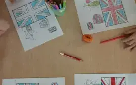 karty pracy z wizerunkiem flagi Wielkiej Brytanii leżą na stoliku na kt&oacute;rym stoją w pojemniku i leżą kredki