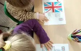 dwie dziewczynki pochylone nad stolikiem kolorują flagi Wielkiej Brytanii