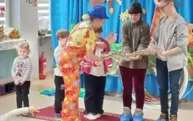 czworo dzieci trzyma węża na rękach przed nimi pani asekuruje zwierzaka obok stoi mała dziewczynka