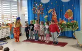 sz&oacute;stka dzieci stoi w rzędzie obok kuca pani w kolorowym ubraniu i niebieskim kapeluszu