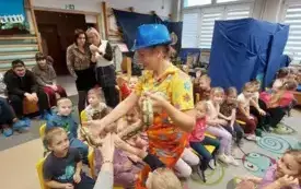 pani w kolorowym ubraniu i niebieskim kapeluszu trzyma węża na rękach i pozwala dotknąć go dzieciom
