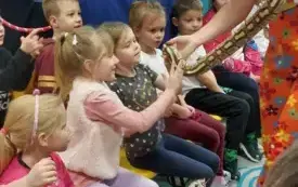 pani w kolorowym ubraniu i niebieskim kapeluszu trzyma węża na rękach i pozwala dotknąć go dzieciom