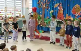 pani w kolorowym ubraniu i peruce wraz z dziećmi stoją w p&oacute;łkolu pani m&oacute;wi coś do mikrofonu