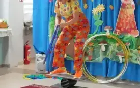 pani w kolorowym ubraniu i peruce stoi na r&oacute;wnoważni i podnosi obręcze