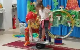 pani w kolorowym ubraniu i peruce ustawia dziewczynkę na r&oacute;wnoważni 