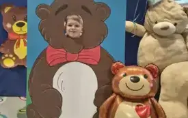 dziecko pozuje do zdjęcia w fotobudce miś widać dużą sylwetkę misia i buzię dziecka obok dekoracja miś balon