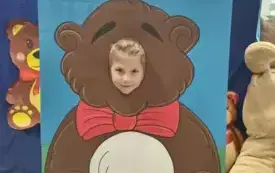 dziecko pozuje do zdjęcia w fotobudce miś widać dużą sylwetkę misia i buzię dziecka obok dekoracja miś balon