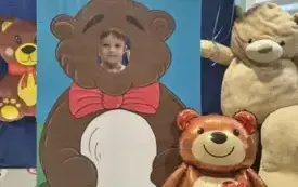 dziecko pozuje do zdjęcia w fotobudce miś widać dużą sylwetkę misia i buzię dziecka obok dekoracja miś balon