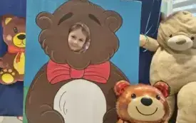 dziecko pozuje do zdjęcia w fotobudce miś widać dużą sylwetkę misia i buzię dziecka obok dekoracja miś balon