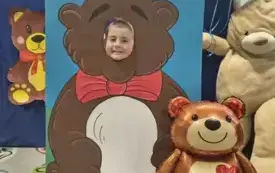 dziecko pozuje do zdjęcia w fotobudce miś widać dużą sylwetkę misia i buzię dziecka obok dekoracja miś balon