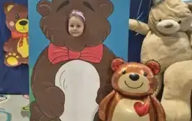 dziecko pozuje do zdjęcia w fotobudce miś widać dużą sylwetkę misia i buzię dziecka obok dekoracja miś balon