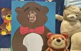 dziecko pozuje do zdjęcia w fotobudce miś widać dużą sylwetkę misia i buzię dziecka obok dekoracja miś balon