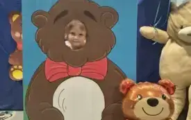 dziecko pozuje do zdjęcia w fotobudce miś widać dużą sylwetkę misia i buzię dziecka obok dekoracja miś balon