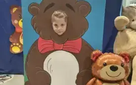 dziecko pozuje do zdjęcia w fotobudce miś widać dużą sylwetkę misia i buzię dziecka obok dekoracja miś balon