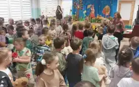 dużo dzieci stoi na sali przed nimi pani w tle inna pani