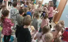 dużo dzieci stoi na sali przed nimi pani w tle inna pani