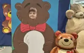 dziecko pozuje do zdjęcia w fotobudce miś widać dużą sylwetkę misia i buzię dziecka obok dekoracja miś balon