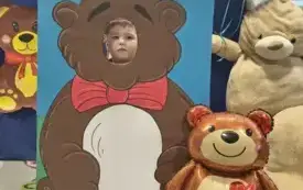 dziecko pozuje do zdjęcia w fotobudce miś widać dużą sylwetkę misia i buzię dziecka obok dekoracja miś balon