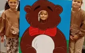 dziecko pozuje do zdjęcia w fotobudce miś widać dużą sylwetkę misia i buzię dziecka po obu stronach stoją dwie dziewczynki w opaskach miś