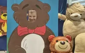 dziecko pozuje do zdjęcia w fotobudce miś widać dużą sylwetkę misia i buzię dziecka obok dekoracja miś balon