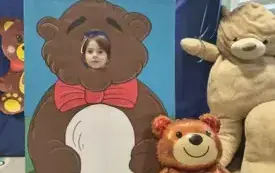 dziecko pozuje do zdjęcia w fotobudce miś widać dużą sylwetkę misia i buzię dziecka obok dekoracja miś balon