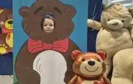 dziecko pozuje do zdjęcia w fotobudce miś widać dużą sylwetkę misia i buzię dziecka obok dekoracja miś balon