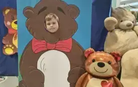 dziecko pozuje do zdjęcia w fotobudce miś widać dużą sylwetkę misia i buzię dziecka obok dekoracja miś balon