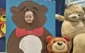 dziecko pozuje do zdjęcia w fotobudce miś widać dużą sylwetkę misia i buzię dziecka obok dekoracja miś balon