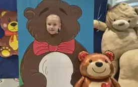dziecko pozuje do zdjęcia w fotobudce miś widać dużą sylwetkę misia i buzię dziecka obok dekoracja miś balon