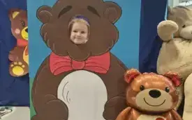 dziecko pozuje do zdjęcia w fotobudce miś widać dużą sylwetkę misia i buzię dziecka obok dekoracja miś balon