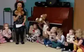dzieci siedzą w kole śr&oacute;d nich na krzesełku siedzi pani z opaską uszy misia wszyscy trzymają pluszowe zabawki