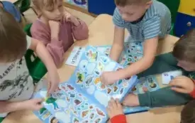 dzieci siedzą przy stoliku i odklejają naklejki z książki z naklejkami